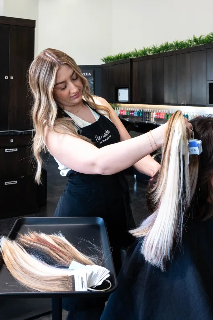 Hali, senior stylist at Panache Hair Studio & Day Spa, specializing in Hair Extensions, Lived in Hair color, Blonding & Makeup. She is holding up hair extension options for a client to select from, finding the perfect match, for your natural, biological hair.
