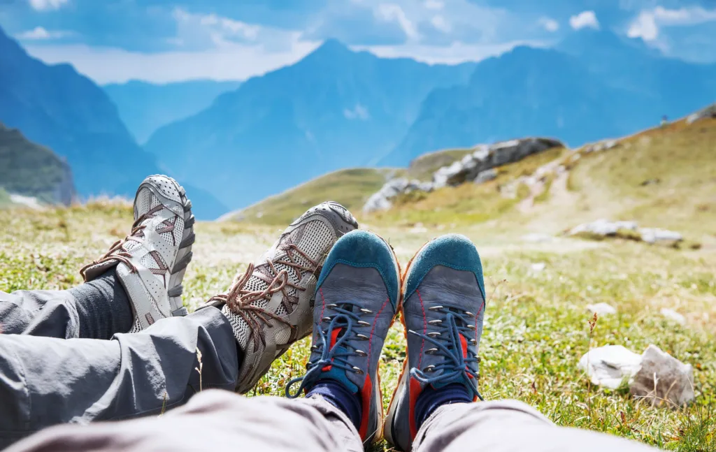Two hiker's feet, wearing hiking boots on an Idaho mountain trail. Examining common foot problems, like cracked heels, dead skin cells, and how to prevent ingrown toenails with pedicure spa treatments at Panache Hair Studio & Day Spa in Meridian, ID.