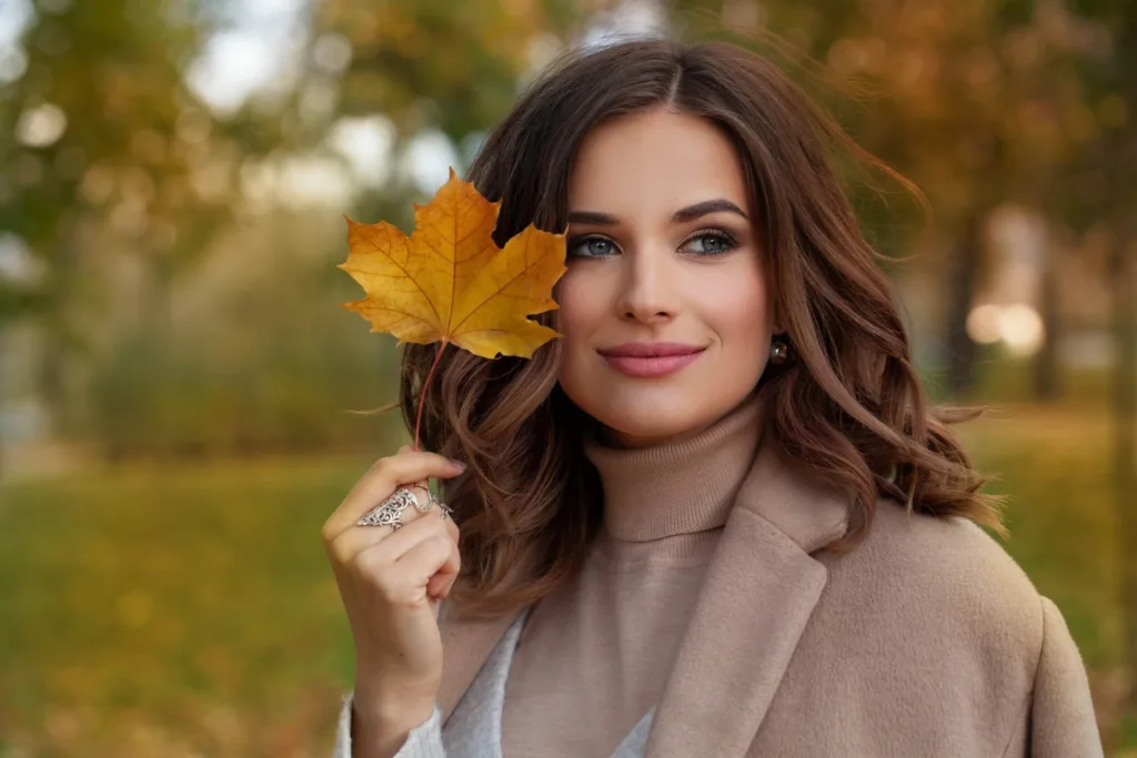 Happy autumn woman with fall yellow maple leaf portrait, showing fall hair color trends. Get the latest styles and color treatments from Panache Hair Studio in the Village at Meridian, Idaho.