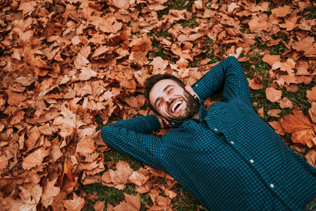 A man laying in a pile of Autumn leaves outside his Eagle, ID home. He has a well-kept beard and hair after visiting Panache Barber on Eagle Road, in The Village at Meridian. 